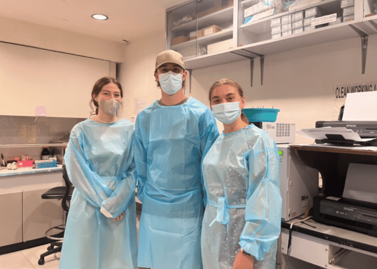 Three students stand in a hospital in the Philippines wearing scrubs and surgical masks