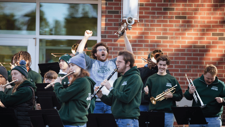 Titan Pep Band playing in front of State Farm Hall with one student raising a trumpet and cheering