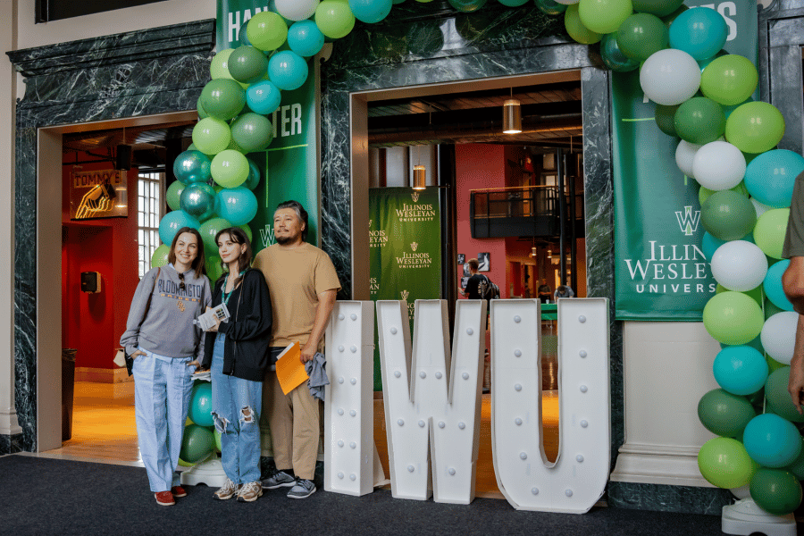 Student with family standing in front of IWU sign and balloons