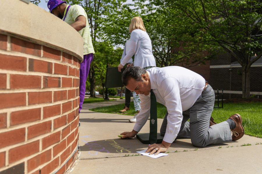 IWU President Sheahon Zenger writes student names in chalk around Aspiration Fountain