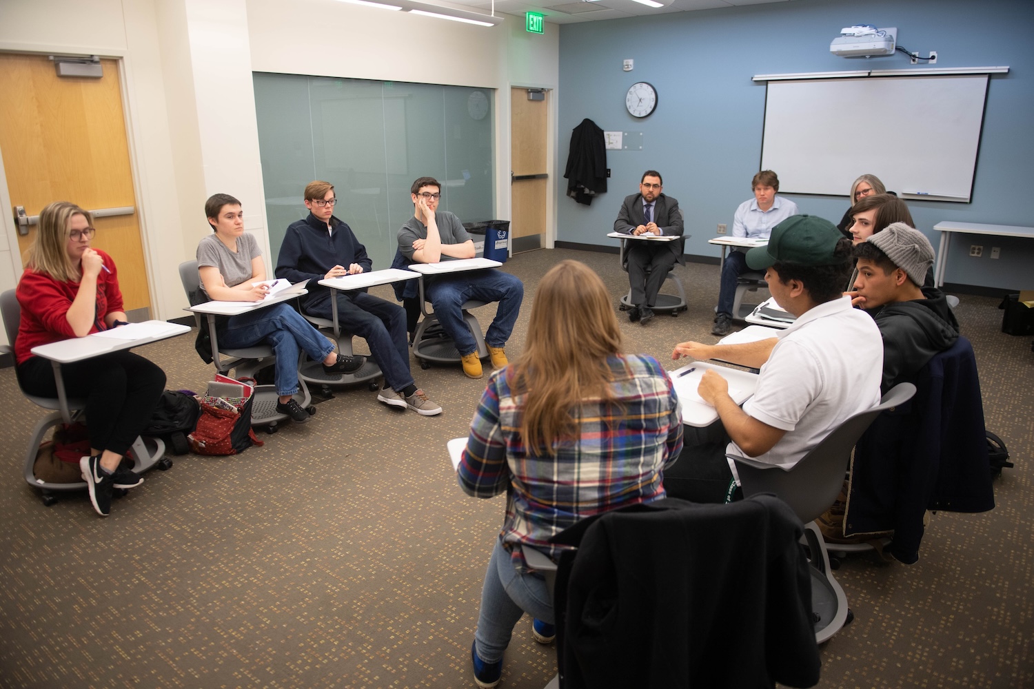 individuals seated at desks in a circle in a classroom