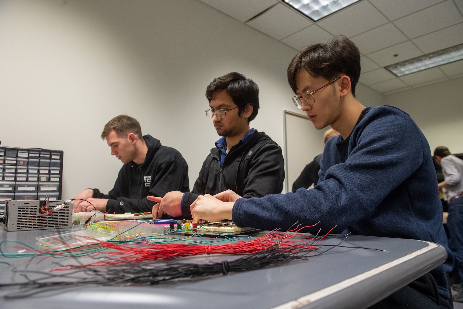 people seated at a large desk/table working with circuitry and wiring